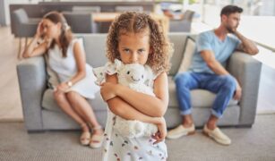 fetita-cu-jucarie-in-brate-mama-si-tata-pe canapea-gri