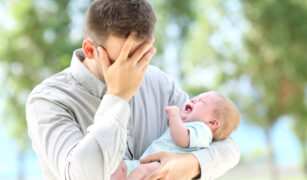 tata furios cu mana la ochi care tine in brate un copil care plange