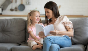 copil vesel citeste dintr-o carte alaturi de mama lui