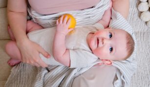 bebelus in bratele mamei care tine in mana o portocala