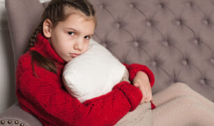 fetita care sta pe canapea si imbratiseaza o perna